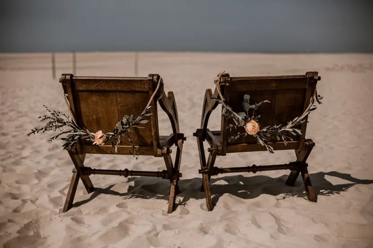 Zwei dunkle Brautpaarstühle mit Olivenzweigen im Sand am Strand