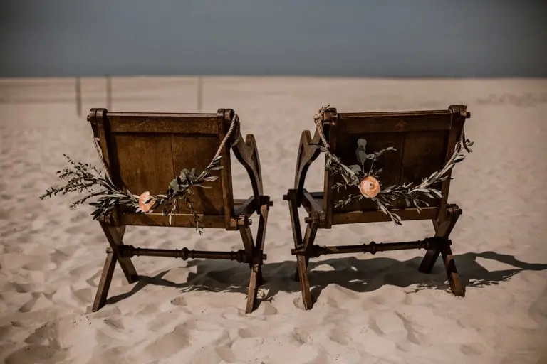 Brautpaarstühle mieten Zwei dunkle Brautpaarstühle mit Olivenzweigen im Sand am Strand