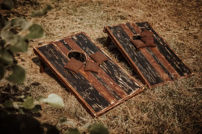 Cornhole mieten Zwei Cornhole Bretter aus dunklem Holz mit Wurfsäckchen auf Stroh