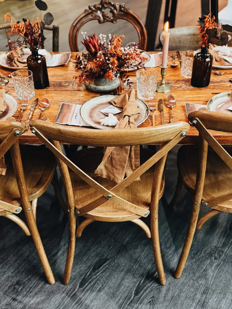 Crossbackchairs mieten Crossbackchairs aus hellem Holz mit Lederriemen an einer gedeckten Holztafel mit Trockenblumen