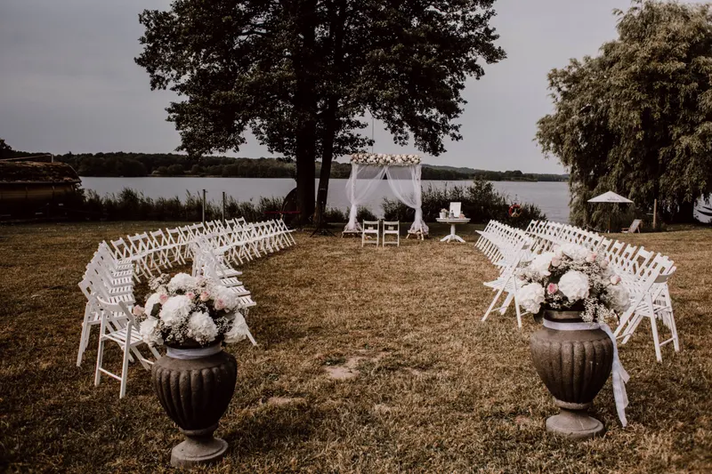 Weiße Stühle am See Weiße Klappstühle in Reihen am Seeufer mit Blumenkübeln