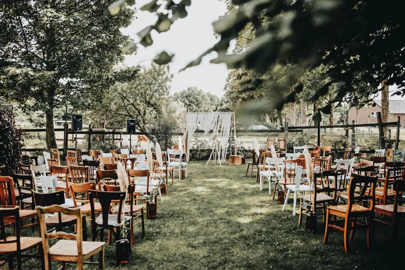Gartenhochzeit Lange Holztafeln mit Stühlen unter Bäumen bei einer Gartenhochzeit