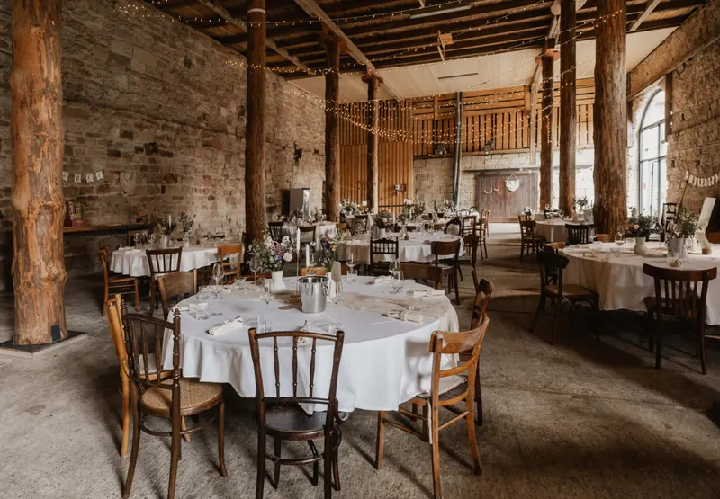 Rundtische mit weißen Decken und Holzstühlen in einer alten Halle