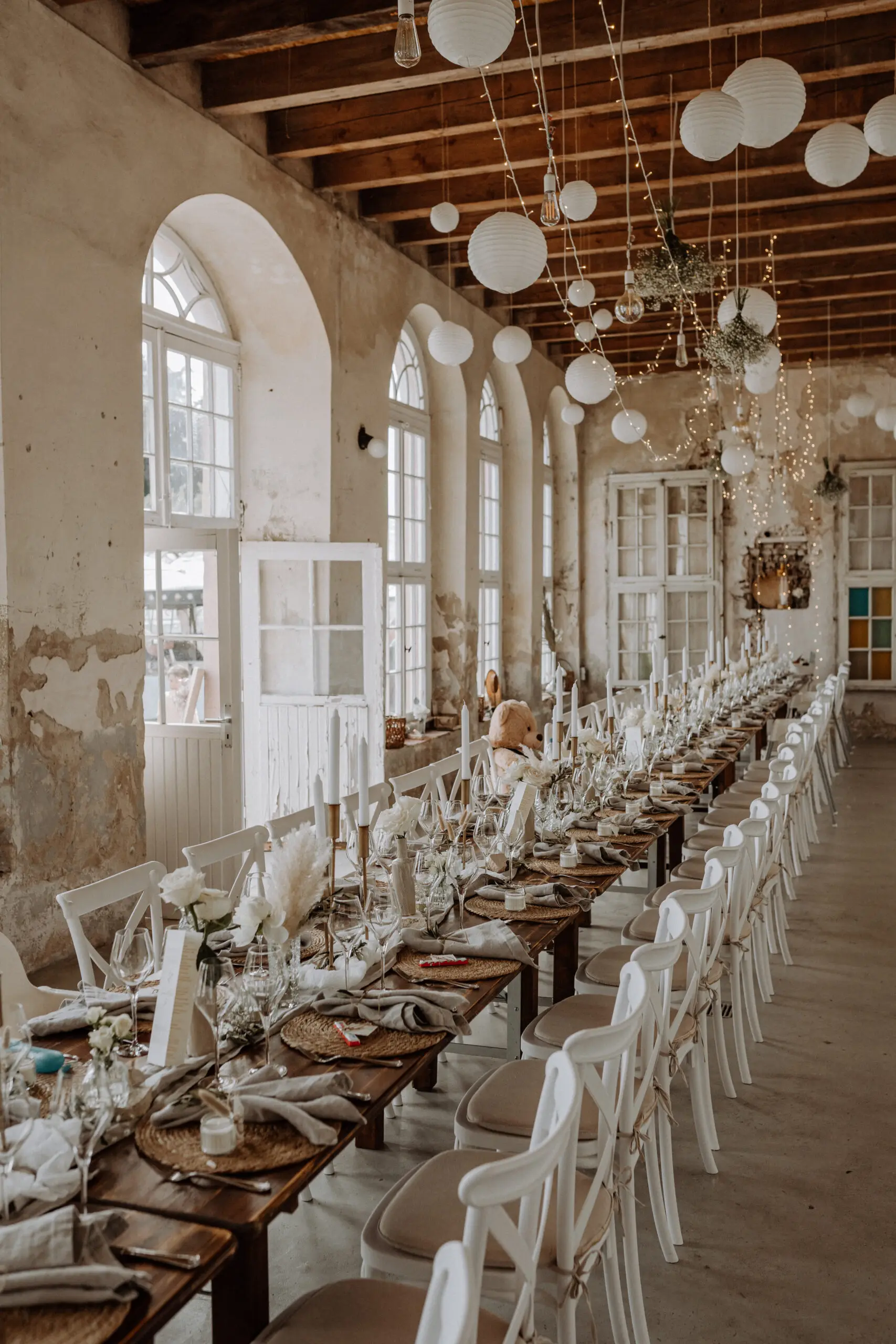 Helle Halle mit Tafel Lange Tafel mit weißen Stühlen in einer hellen Halle mit Rundbogenfenstern