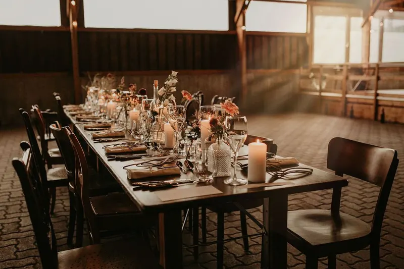 Scheunenhochzeit Gedeckte Holztafel mit Kerzen und dunklen Stühlen in einer Scheune