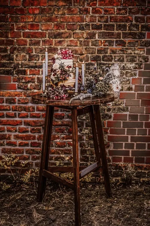 Stehtisch mieten Dunkler Holzstehtisch mit Blumen vor einer Backsteinwand