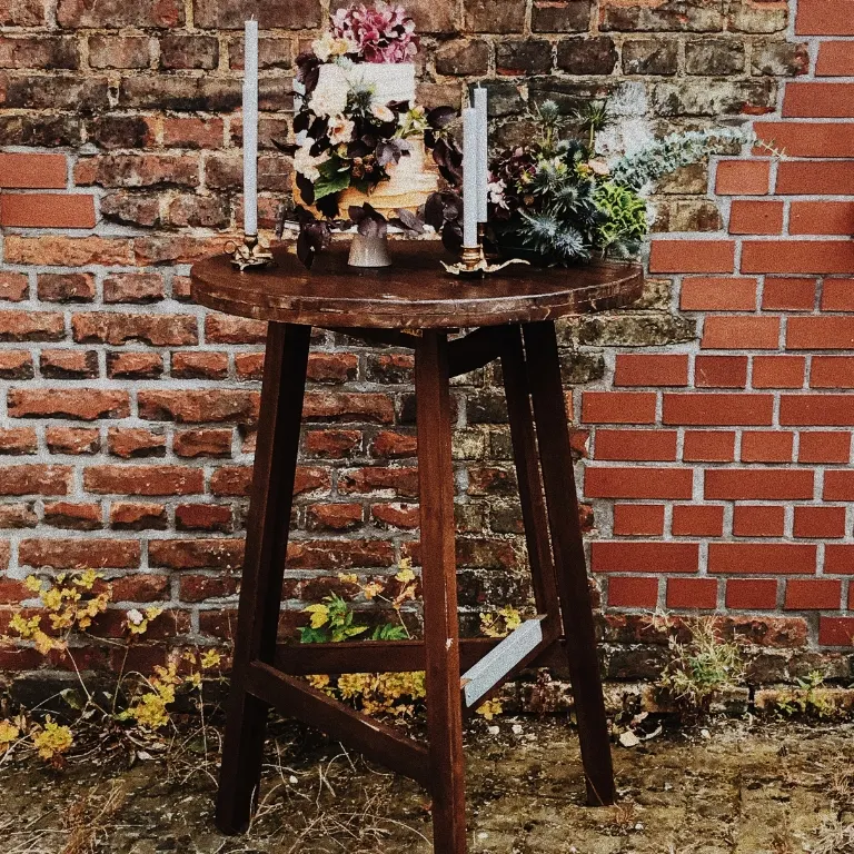 Stehtisch mit Torte Stehtisch aus dunklem Holz mit Hochzeitstorte vor Backstein