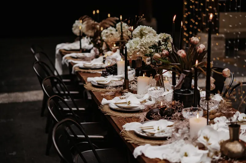 Dunkle Tafel Dunkle Tafel mit weißen Blumen, Kerzen und schwarzen Stühlen
