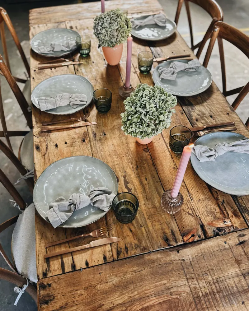 Tisch Finca mieten Tisch Finca aus grobem Holz mit grauen Tellern, Buchsbaum und rosa Kerzen